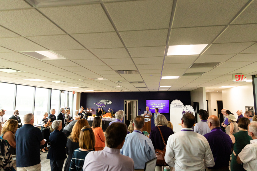 People speak at a podium in front of a large group of people.