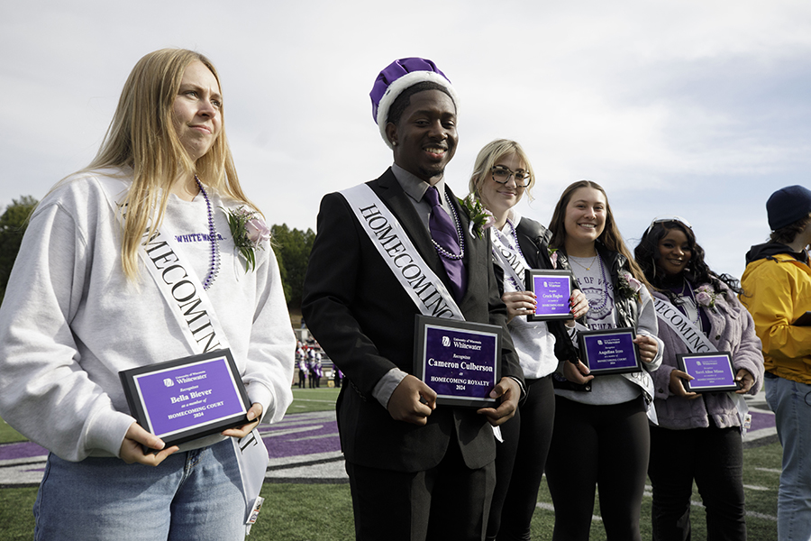 Students line up on the football field and hold plaques and wearing sashes that say Homecoming.