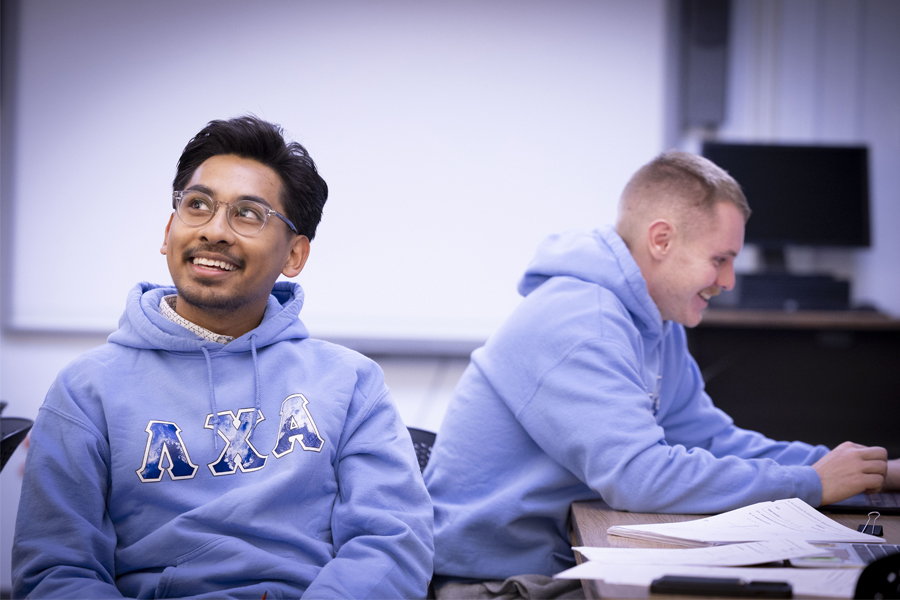 Two smiling men sit at classroom table.