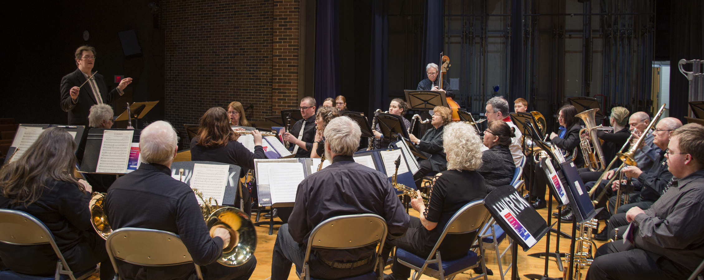 A faculty member in a suit and tie conducts a band as people hold their instruments.