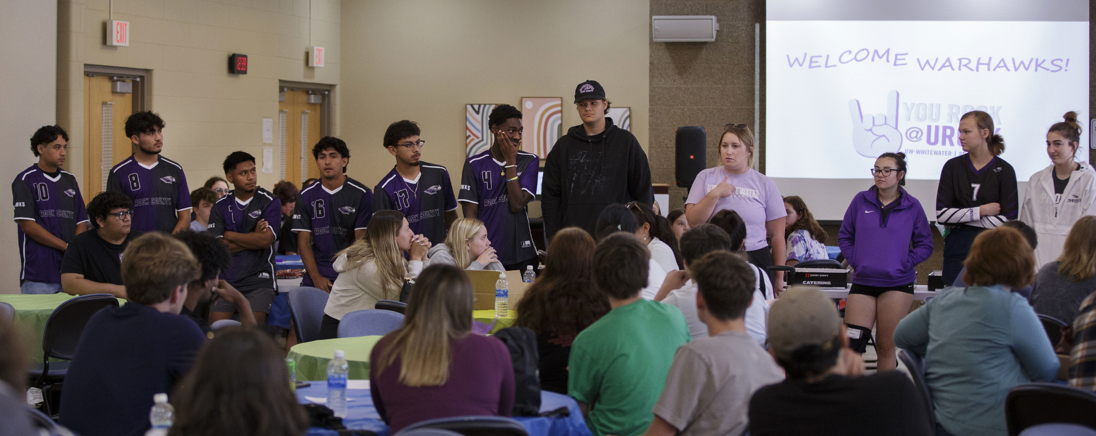 The URock men's soccer and women's volleyball team speak in front of a crowd of their peers.