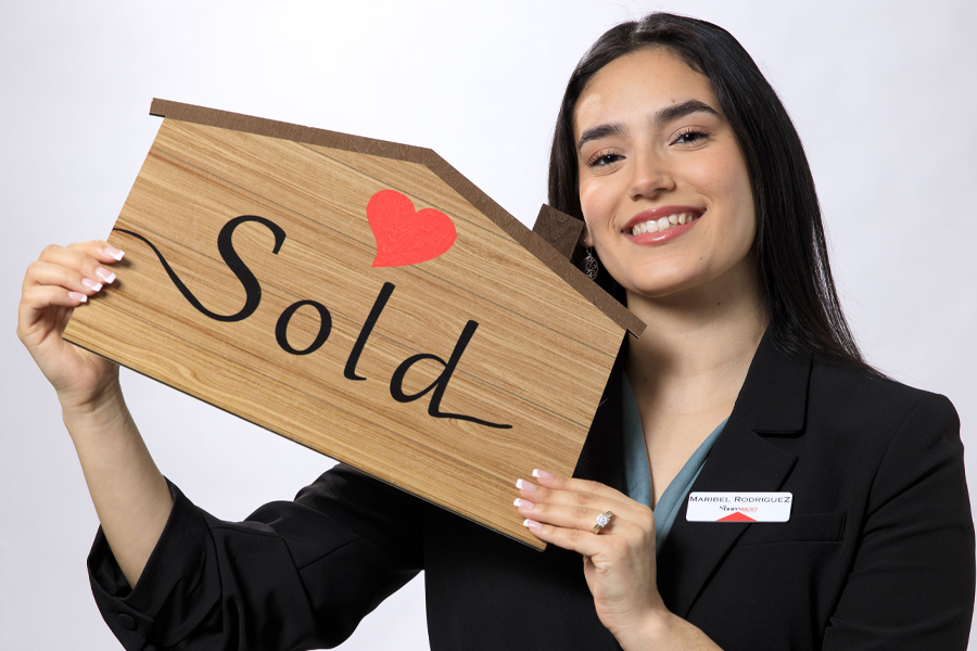 A student wearing a black blazer holds up a wooden sign that says sold.