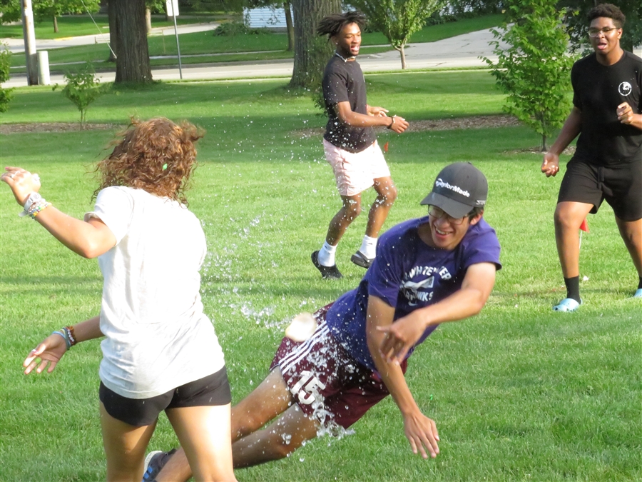 Students playfully throw water at each other outdoors.