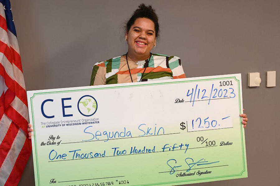 A student holds a large check and smiles at the camera.