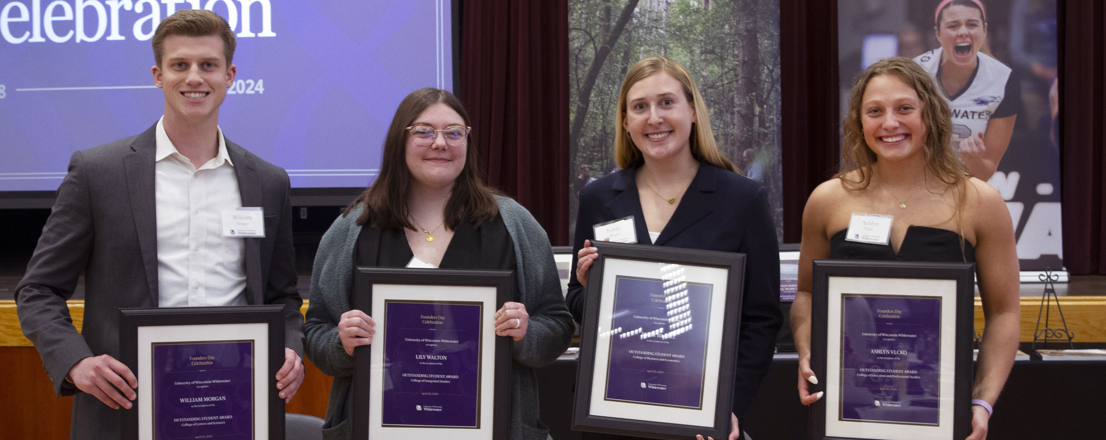 Four students pose together and each are holding a framed award.